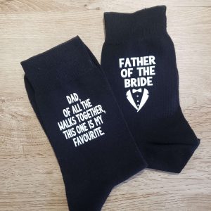 A pair of black cotton socks featuring a fun design: one sock reads “Dad, of all the walks together, this one is my favourite” while the other shows “Father of the Bride/Groom” alongside a tuxedo image