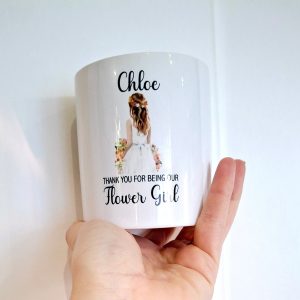 Hand holding a white ceramic money jar with a young girl on holding flowers and personalised with a name and the words thank you for being our flower girl.